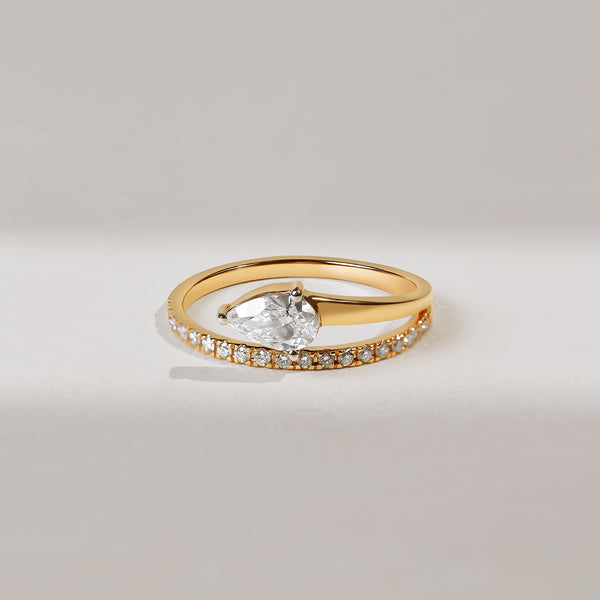 Gold ring with a pear-shaped diamond and smaller stones on a light gray background