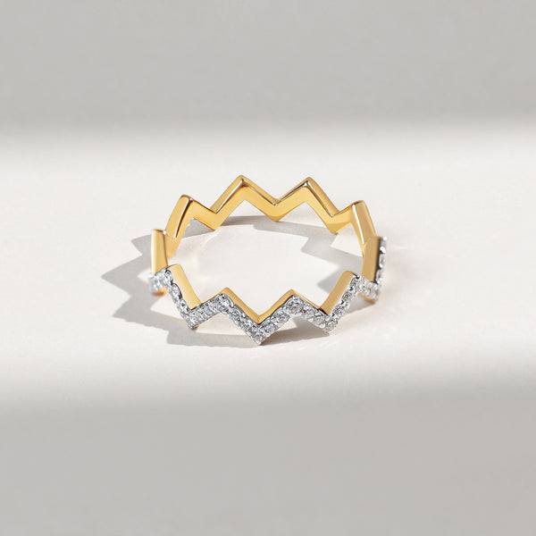 Gold ring with zigzag design and embedded diamonds on a light gray background