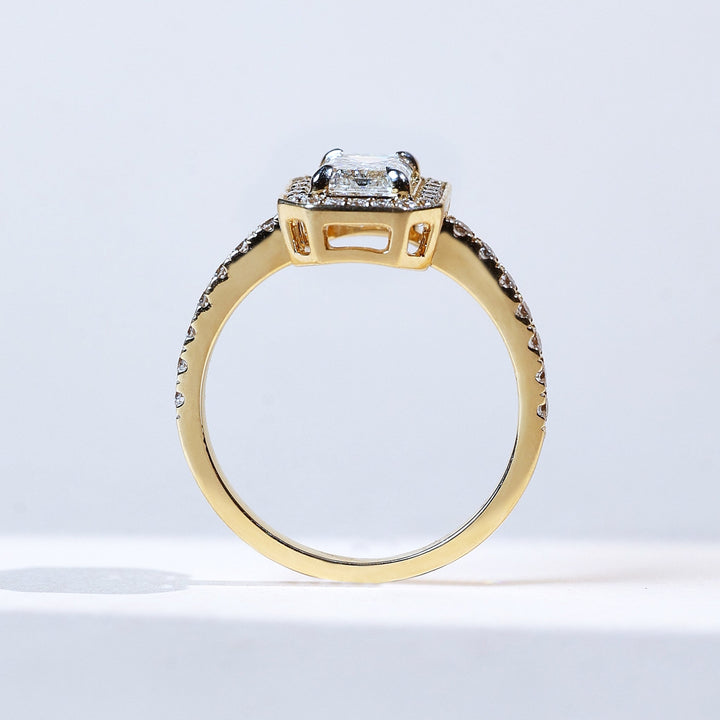 Side profile of emerald-cut halo solitaire diamond ring in yellow gold.