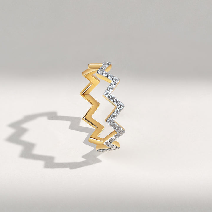 Gold and diamond zigzag ring standing on a light gray background