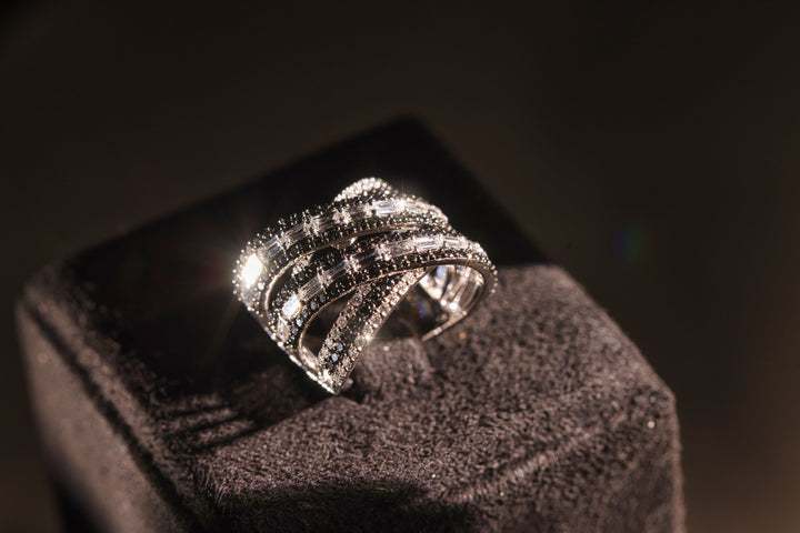 Criss-cross ring with sparkling black and white diamonds in white gold, illuminated against a dark background.