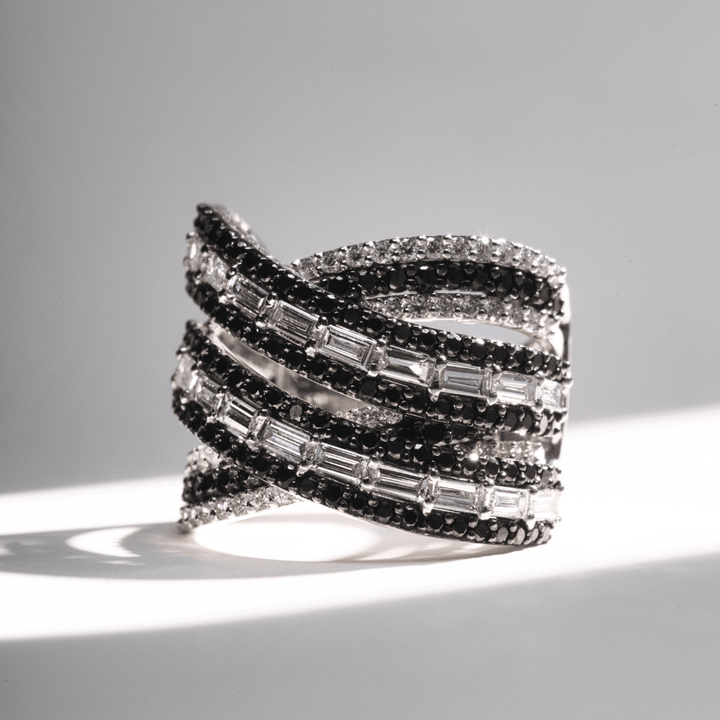 Wide criss-cross ring with alternating rows of black pavé diamonds and baguette-cut white diamonds in white gold.