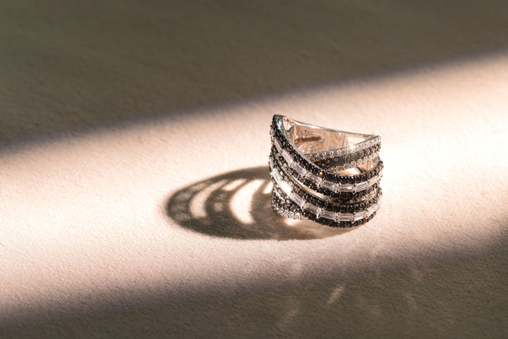 Elegant criss-cross diamond ring with black pavé and baguette-cut white diamonds, softly lit for a warm shimmer.
