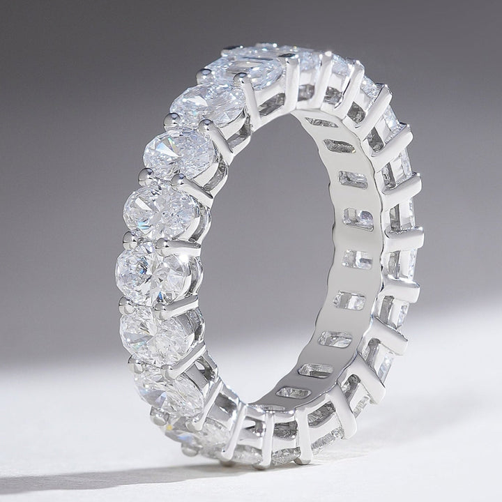 Standing profile of white gold eternity band with alternating oval and emerald-cut diamonds in a prong setting.