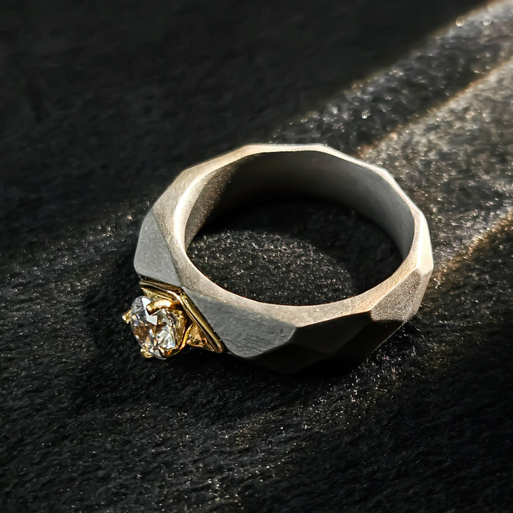 0.5 Ct Helios Titanium Ring placed flat on a black textured surface, showing faceted titanium design and yellow-gold diamond mount — flatlay view.
