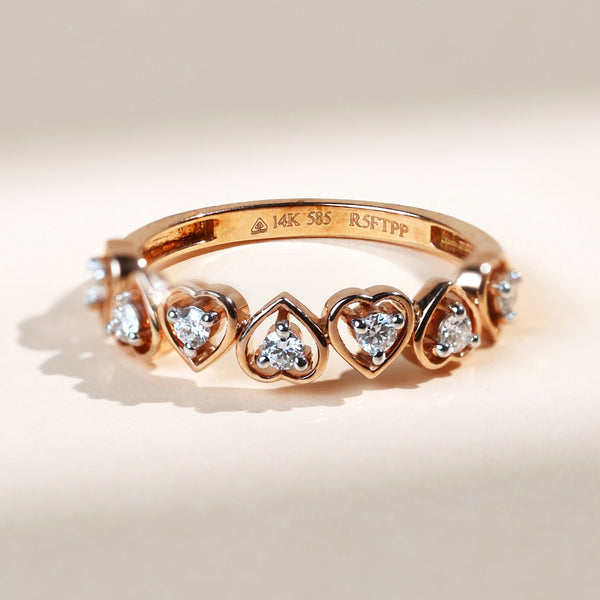 Close-up of rose gold ring with diamond-studded heart motifs.