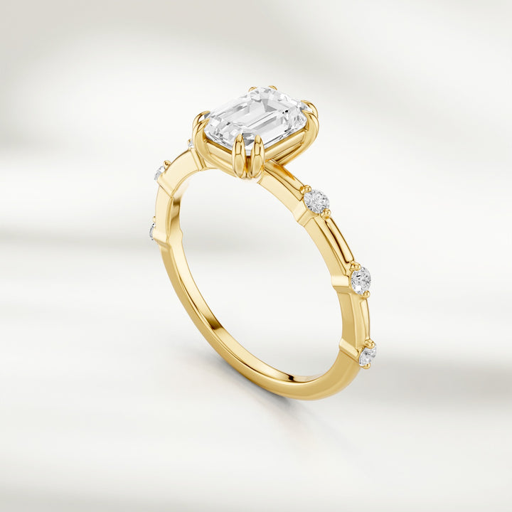 Angled view of 18K yellow gold band featuring a radiant emerald-cut diamond and round diamond stations.