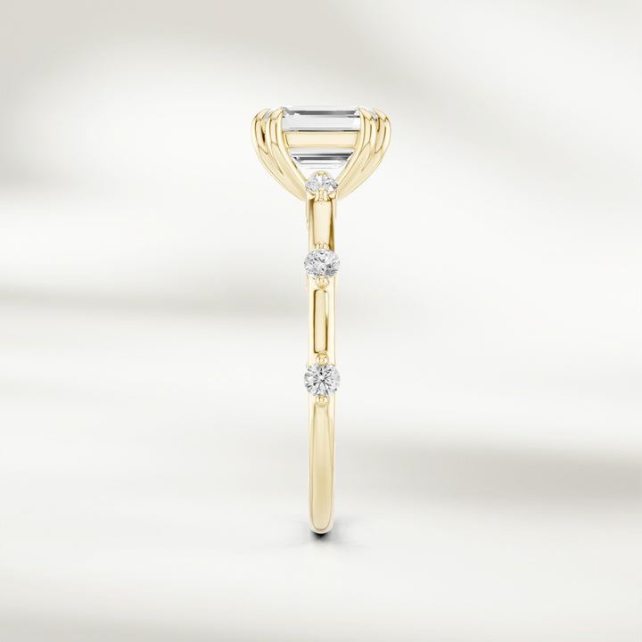 Side profile of 18K yellow gold solitaire ring with a raised emerald-cut diamond and delicate round diamond accents.