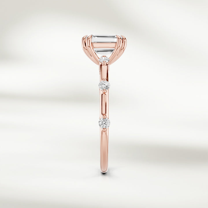 Side profile of 18K yellow gold solitaire ring with a raised emerald-cut diamond and delicate round diamond accents.