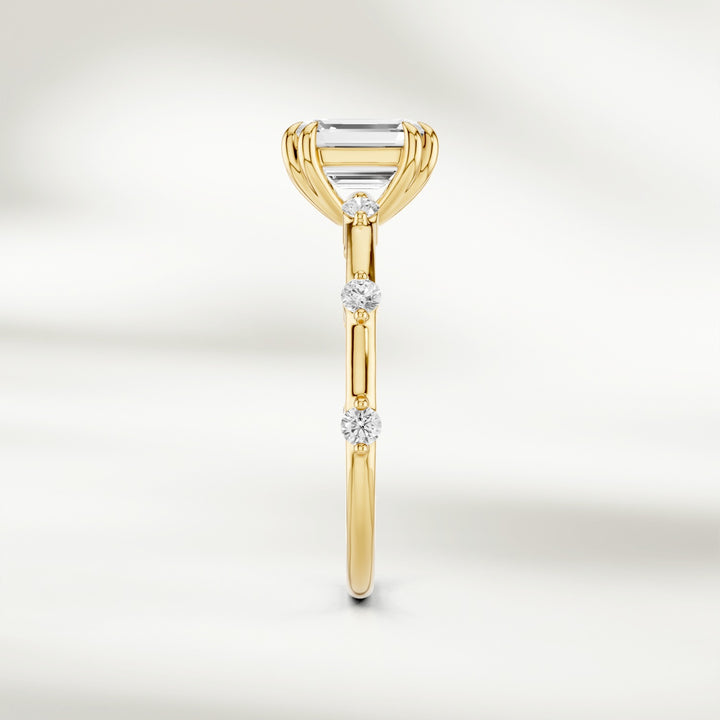 Side profile of 18K yellow gold solitaire ring with a raised emerald-cut diamond and delicate round diamond accents.