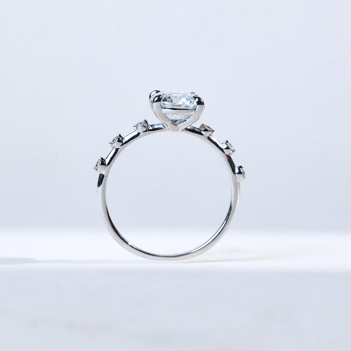 Profile view of round solitaire with scattered diamond accents in band.