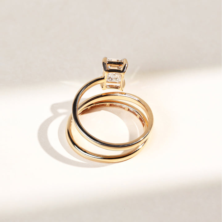 Angled view of gold dual-band cocktail ring with prominent emerald-cut diamond.
